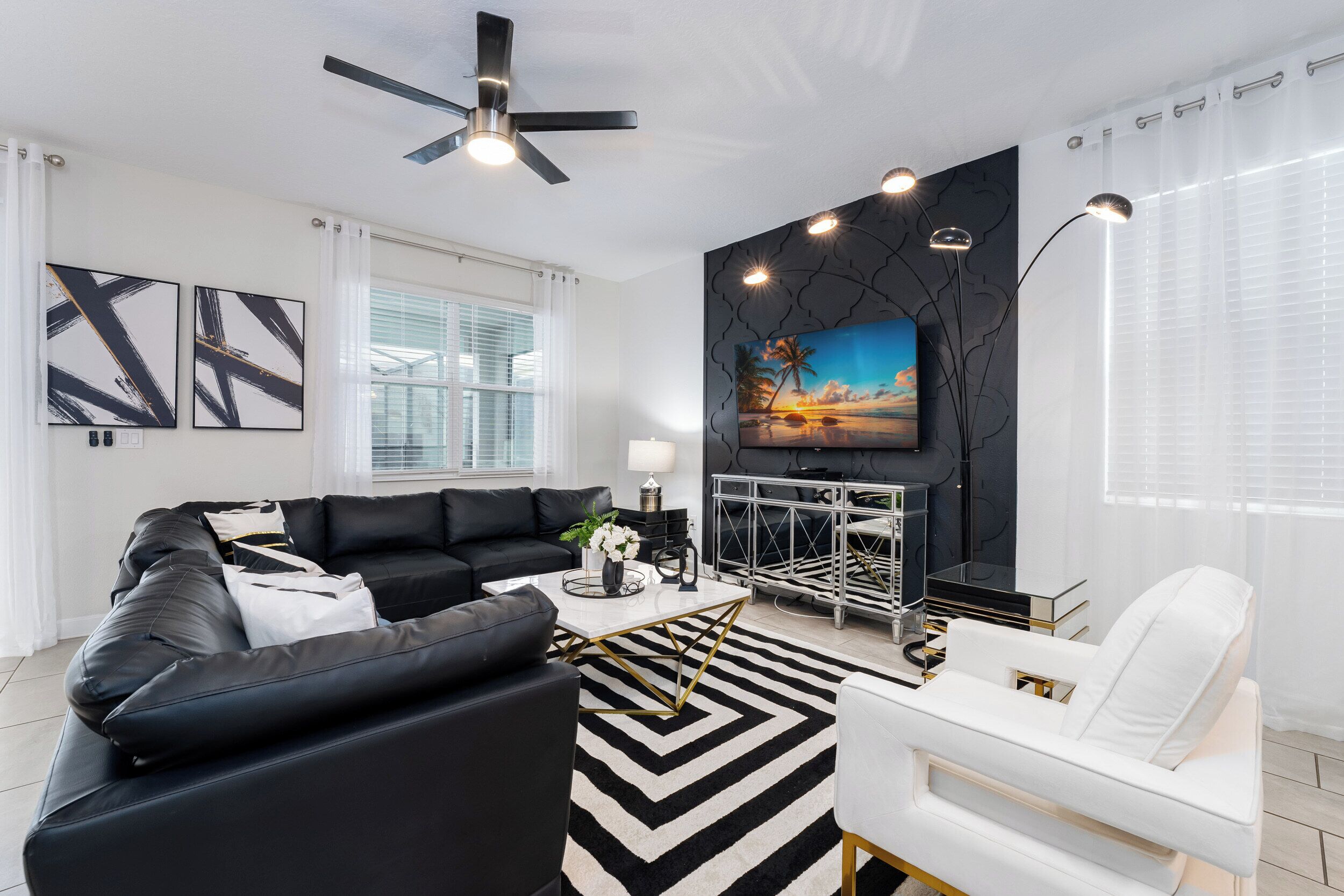 Una sala de estar moderna con un conjunto de sofá y sillones blanco y negro, un sillón blanco, una mesa de centro y un televisor montado en una pared de acento negra.