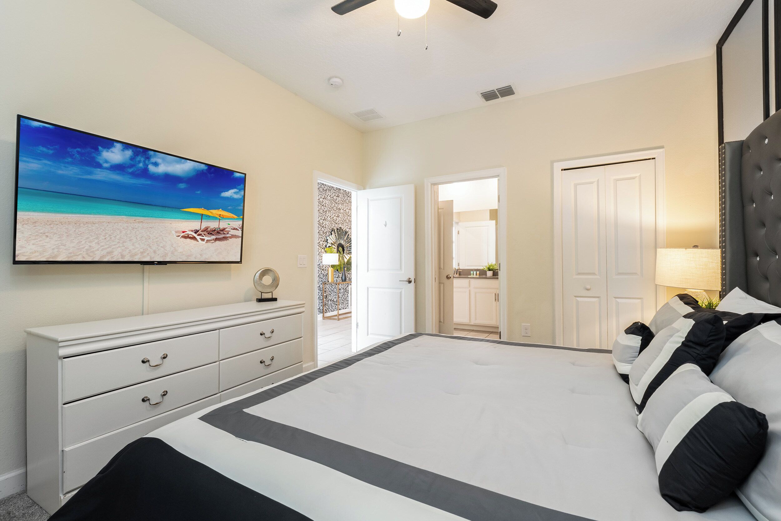 A bedroom with a large bed, a TV on the wall, and a door leading to another room.