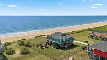 A beachfront property with a large house featuring a balcony, a deck, and a view of the ocean.