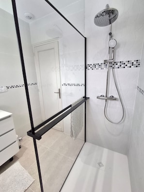 A modern bathroom with a glass partition, a shower with a handheld showerhead, and a white sink.