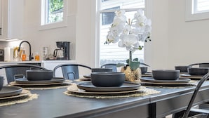 Een eettafel gedekt met zwarte kommen en borden, een vaas met witte orchideeën, en een koffiezetapparaat op de achtergrond.