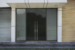 A modern building entrance with a glass door and a metal shutter to the left. - Classic Krishna Inn (Prayagraj)