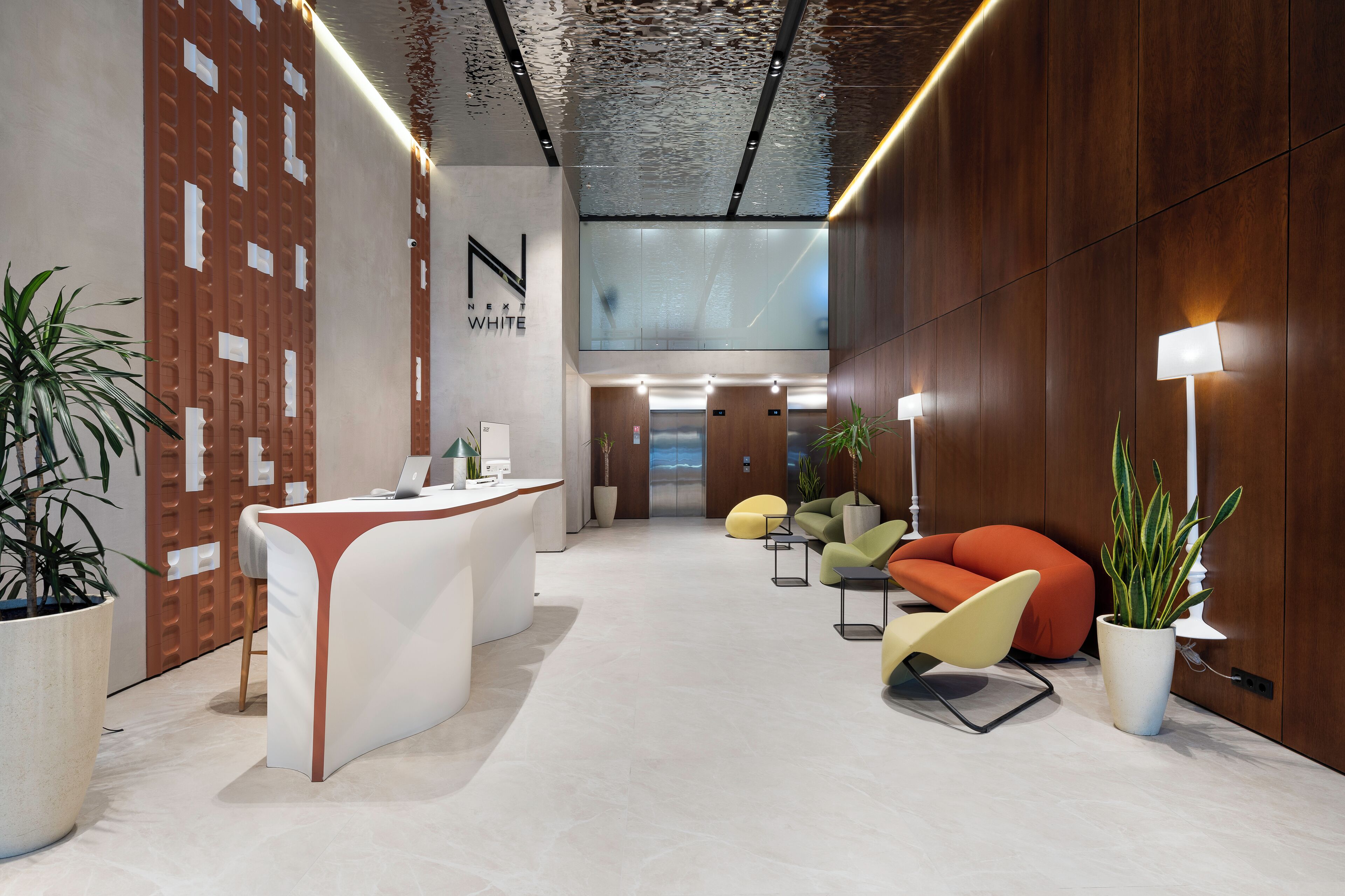 A modern reception area with a reception desk, seating, and potted plants.