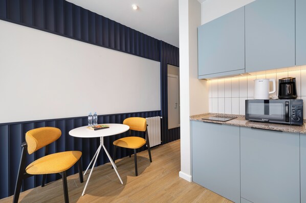 A modern kitchen with a microwave, coffee maker, and a small dining area with a table and chairs. - Next White Aparthotel Official (Batumi)