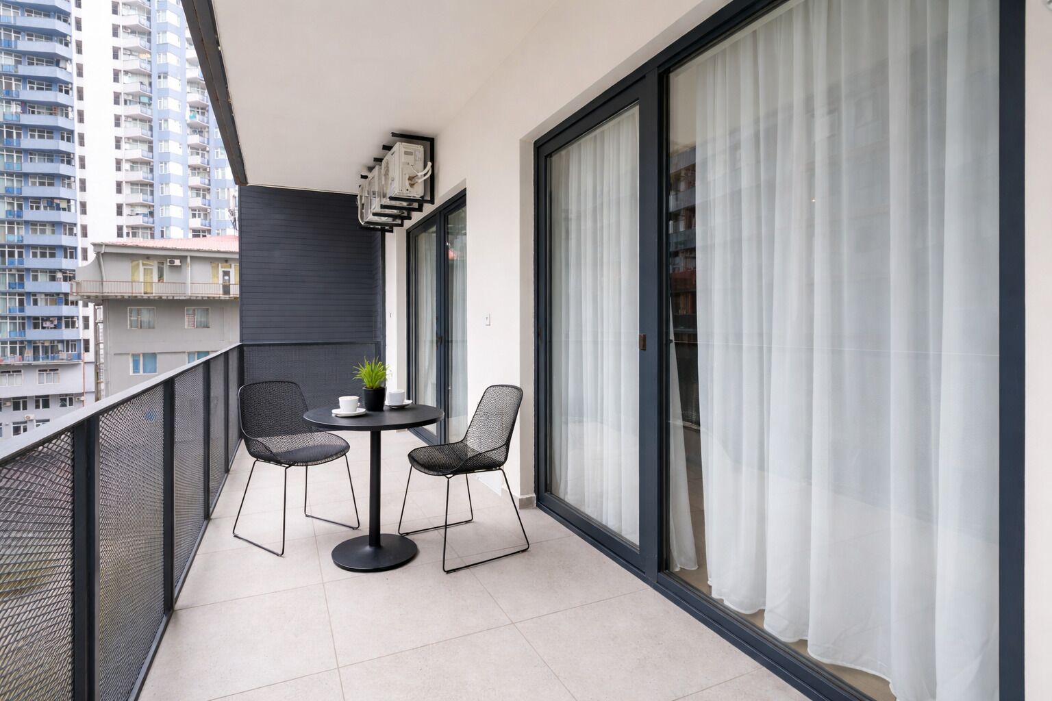 A balcony with a table and chairs, a potted plant, and a view of the cityscape.