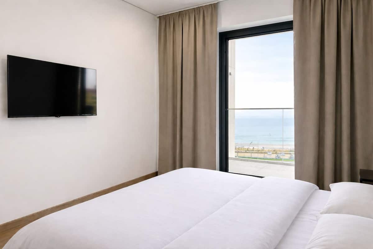 A hotel room with a bed, a flat-screen TV, and a balcony with curtains.