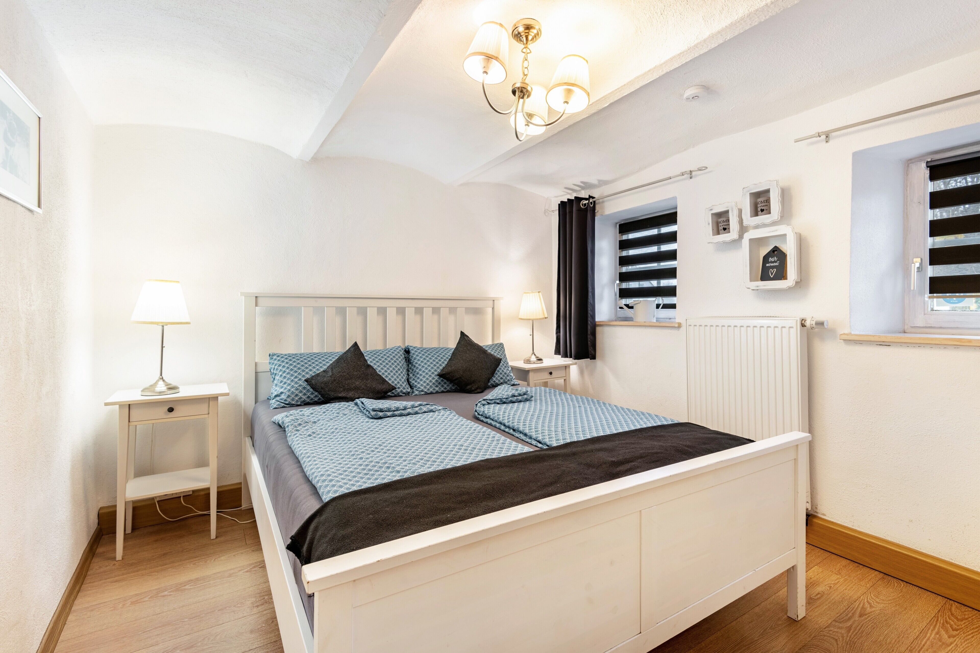 A bedroom with a bed, bedside tables, a lamp, a radiator, and a window with shutters.