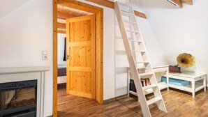 Un dormitorio tipo loft con puerta de madera, escalera blanca, chimenea y una pequeña mesa con libros y un objeto decorativo.