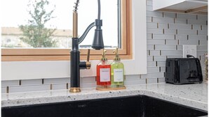Uma cozinha com uma torneira moderna, uma janela e duas embalagens de sabonete no balcão.