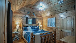 Un dormitorio de cabaña de madera con una cama de madera, dos lámparas de noche, una ventana con cortinas y una puerta de madera.