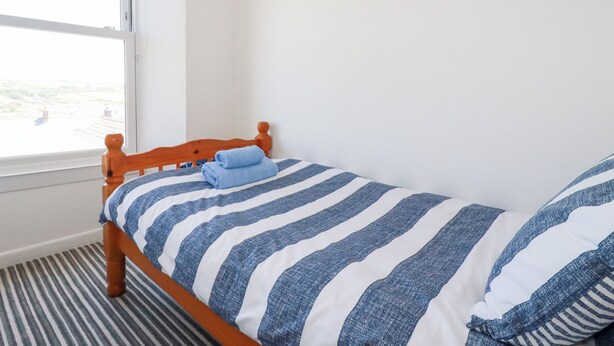 A bedroom with a wooden bed, striped bedding, a window with a view, and a painting on the wall. - Tregundy Farmhouse (Perranporth)