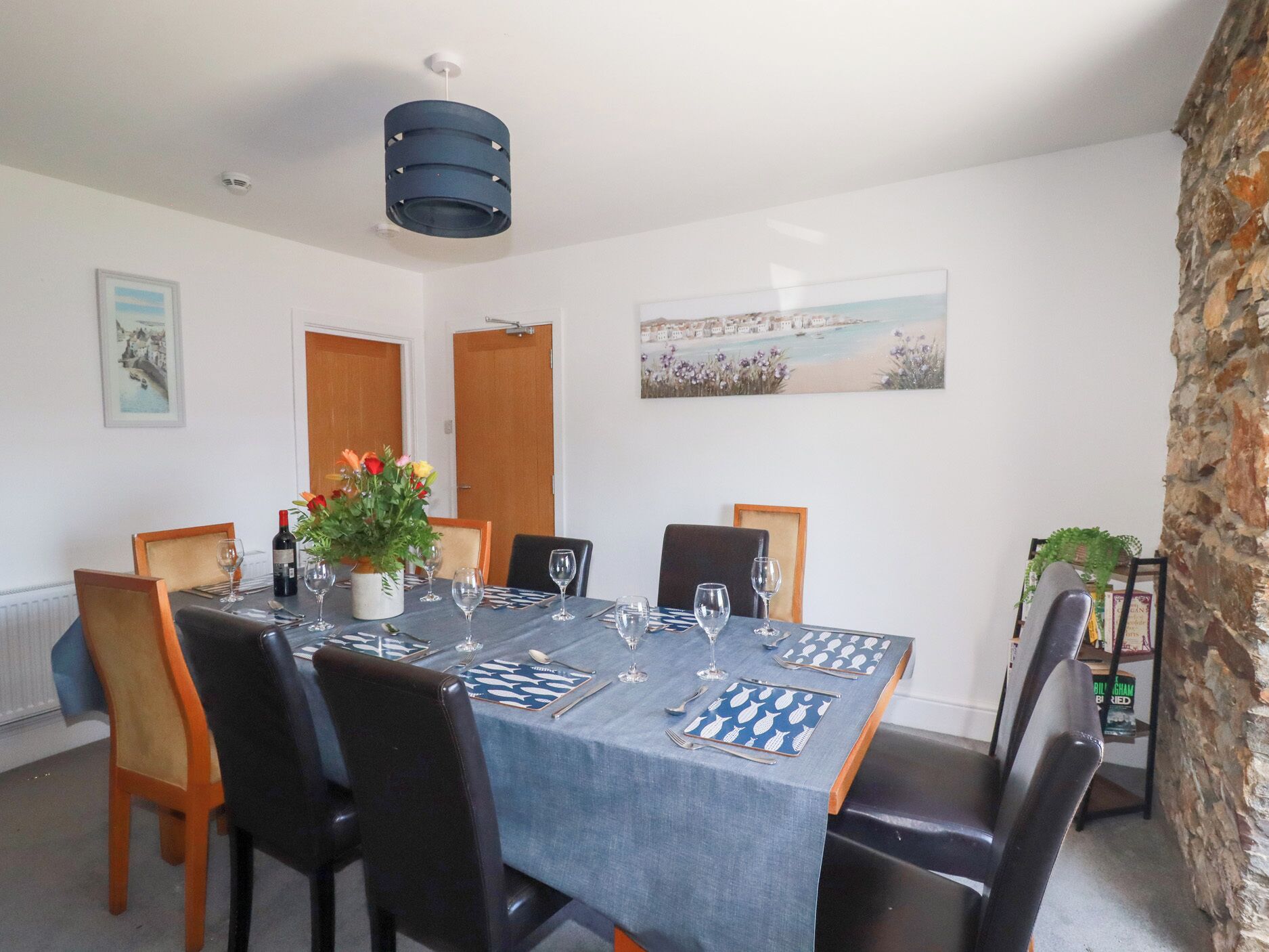 A dining room with a table set for six, chairs, a vase of flowers, and a painting on the wall.