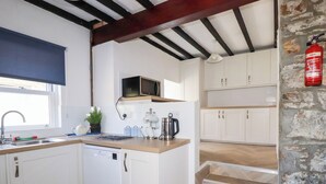 A compact kitchen with white cabinets, a microwave, a kettle, and a fire extinguisher. - Tregundy Farmhouse (Perranporth)