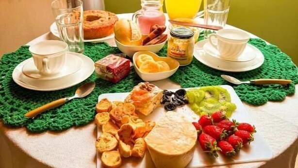 Egy reggelizőasztal, melyen sokféle étel és ital található, és ahonnan zöld tájra nyílik kilátás.