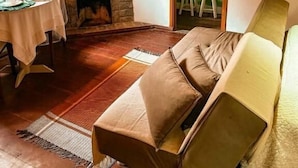 Egy hangulatos szoba kandallóval, egy kényelmes kanapéval, egy két személyre megterített étkezőasztallal és egy a falra szerelt televízióval.