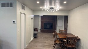 A spacious dining area with a wooden table and chairs, a fireplace, and a modern ceiling light fixture.