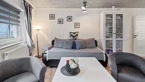 A modern room with a bed, a sofa, a dining table with a flower centerpiece, a lamp, and a cabinet with glass doors. - Apartment 'Ilmhaus 2' with Wi-Fi (Gaden bei Pförring)