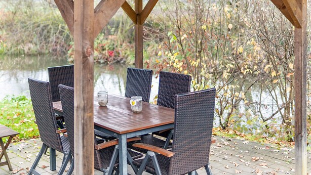 An outdoor wooden pergola with a table and chairs, overlooking a body of water and surrounded by trees. - Apartment 'Ilmhaus 2' with Wi-Fi (Gaden bei Pförring)