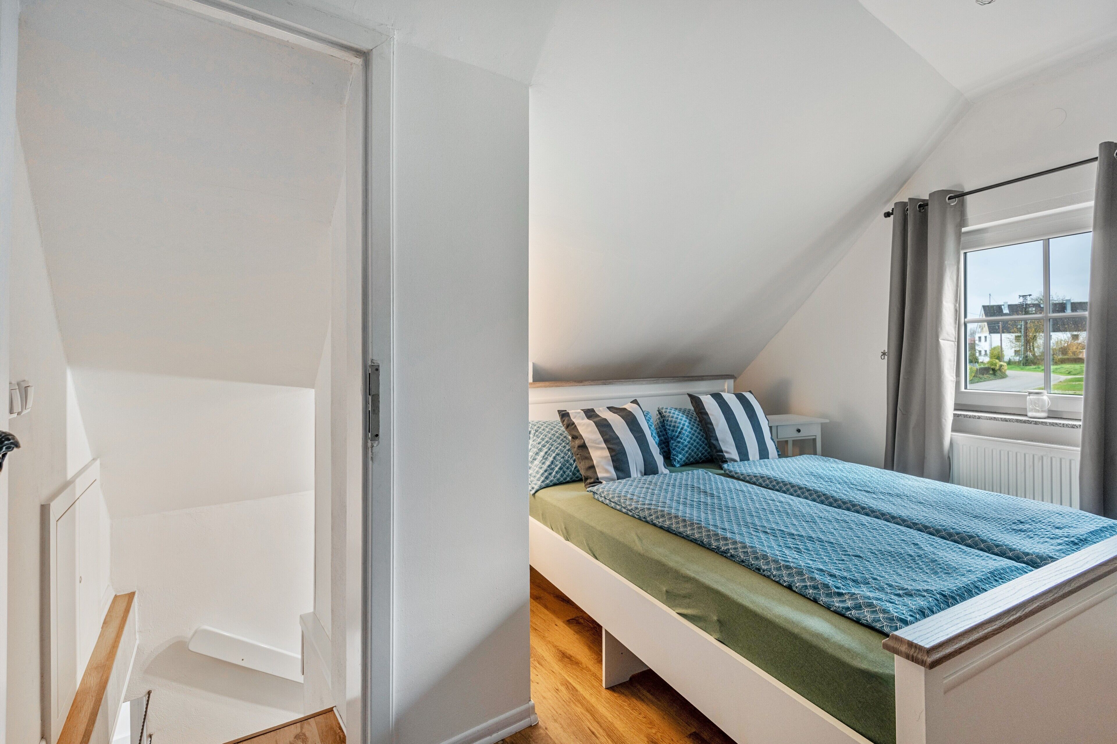 Ein Schlafzimmer mit einem Bett, einem Fenster mit Vorhängen, einem Heizkörper und einer Tür.