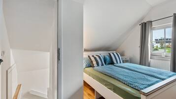 Ein Schlafzimmer mit einem Bett, einem Fenster mit Vorhängen, einem Heizkörper und einer Tür.