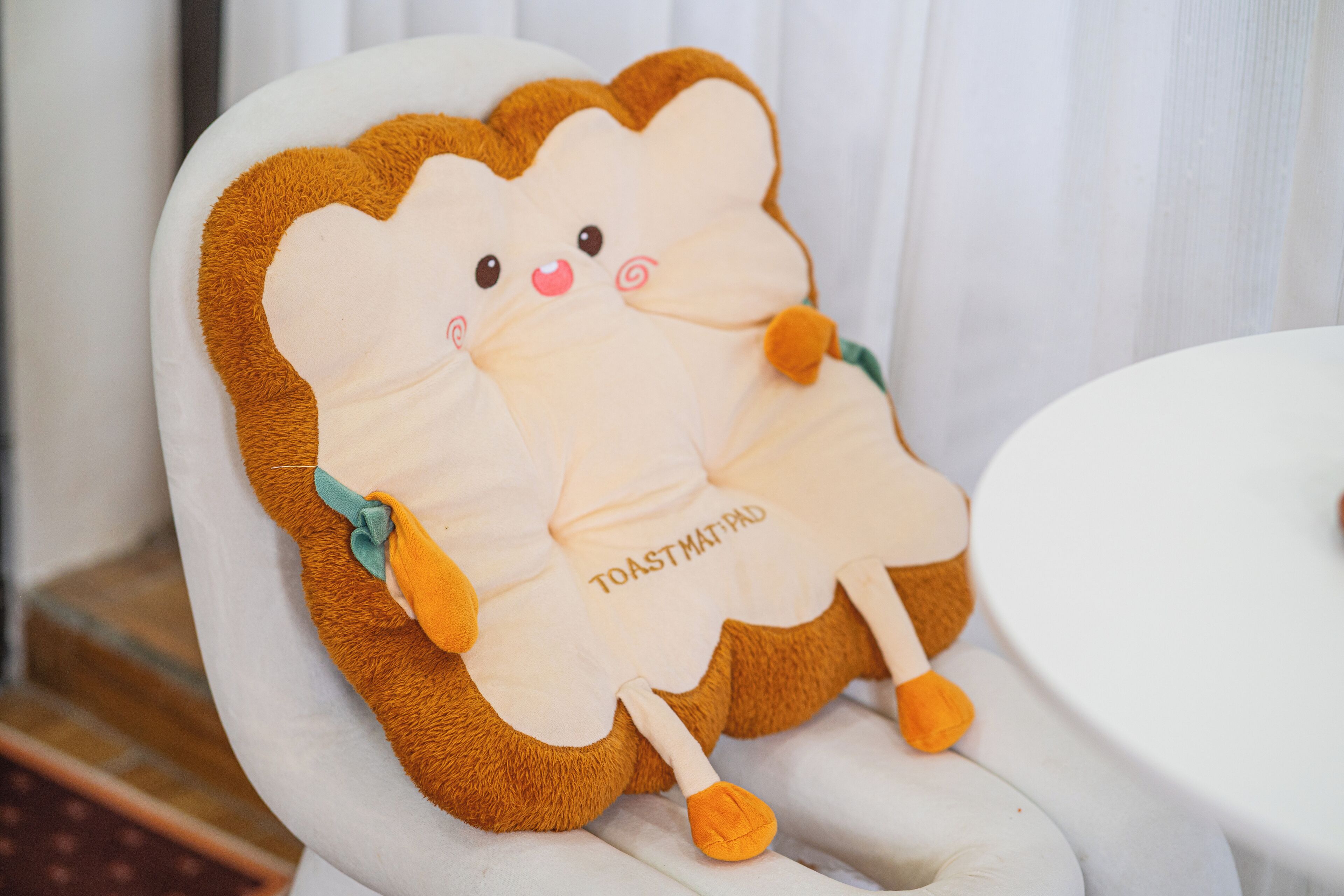 A plush toy resembling toast with a cute face, sitting on a white chair.