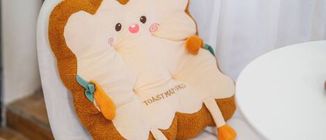 A plush toy resembling toast with a cute face, sitting on a white chair.