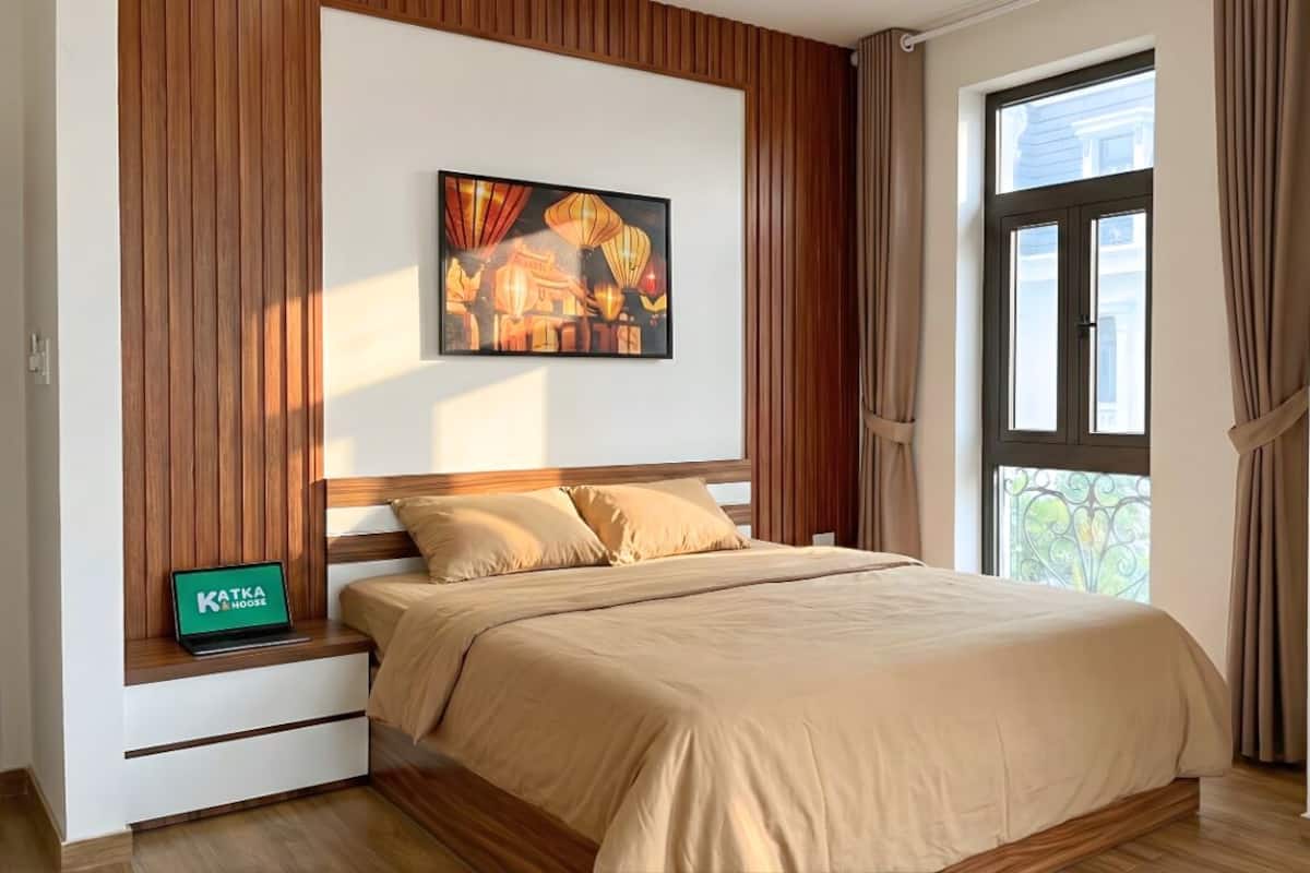 Een slaapkamer met een bed, houten lambrisering, een raam met gordijnen en een schilderij aan de muur.