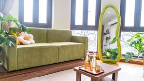 A green sofa, a wooden coffee table with orange juice bottles, and a green mirror in a well-lit room with large windows. - Katka Riverside Homestay Hai Phong (Hai Phong)