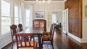 A dining room with a wooden table and chairs, a chandelier, and a view through large windows.