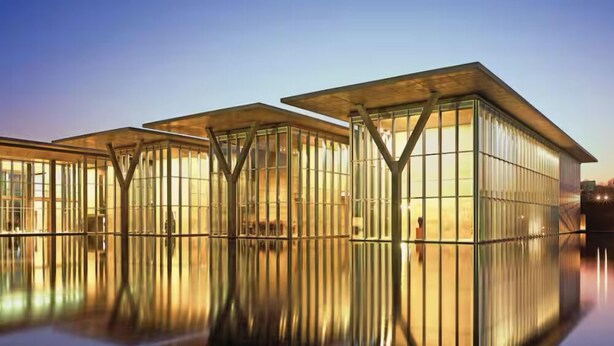 A modern building with a glass facade and a reflective water surface in front.