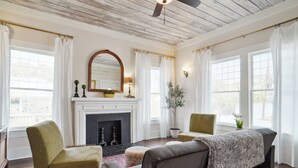 A living room with a fireplace, two armchairs, a sofa, and a large window with curtains.