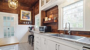 A kitchen with white cabinets, a granite countertop, a microwave, a sink, and a window with a view of trees.