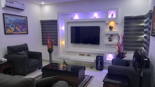 Una sala de estar moderna con un televisor de pantalla plana, sofás oscuros, una mesa de centro y objetos decorativos.