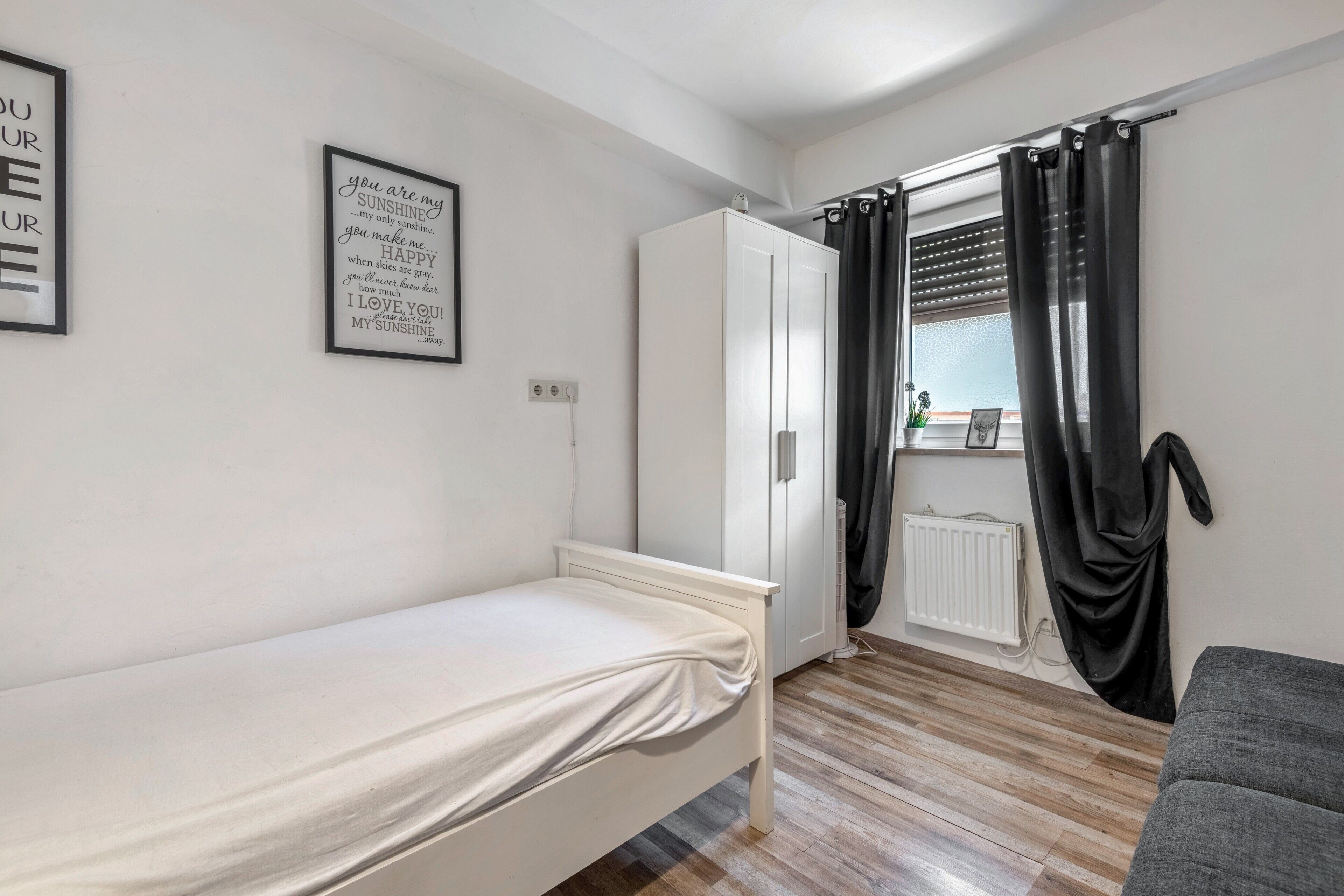A bedroom with a single bed, a wardrobe, a radiator, and a window with curtains.