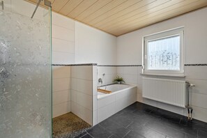 A bathroom with a glass shower enclosure, a bathtub, a window with a view, and a white radiator. - Holiday Home 'Am Limes' with Private Terrace, Private Garden and Wi-Fi (Altmannstein)