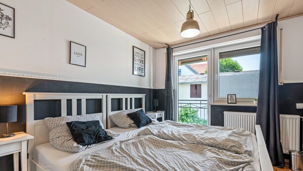 A bedroom with a bed, bedside tables, a window with curtains, and wall art. - Holiday Home 'Am Limes' with Private Terrace, Private Garden and Wi-Fi (Altmannstein)