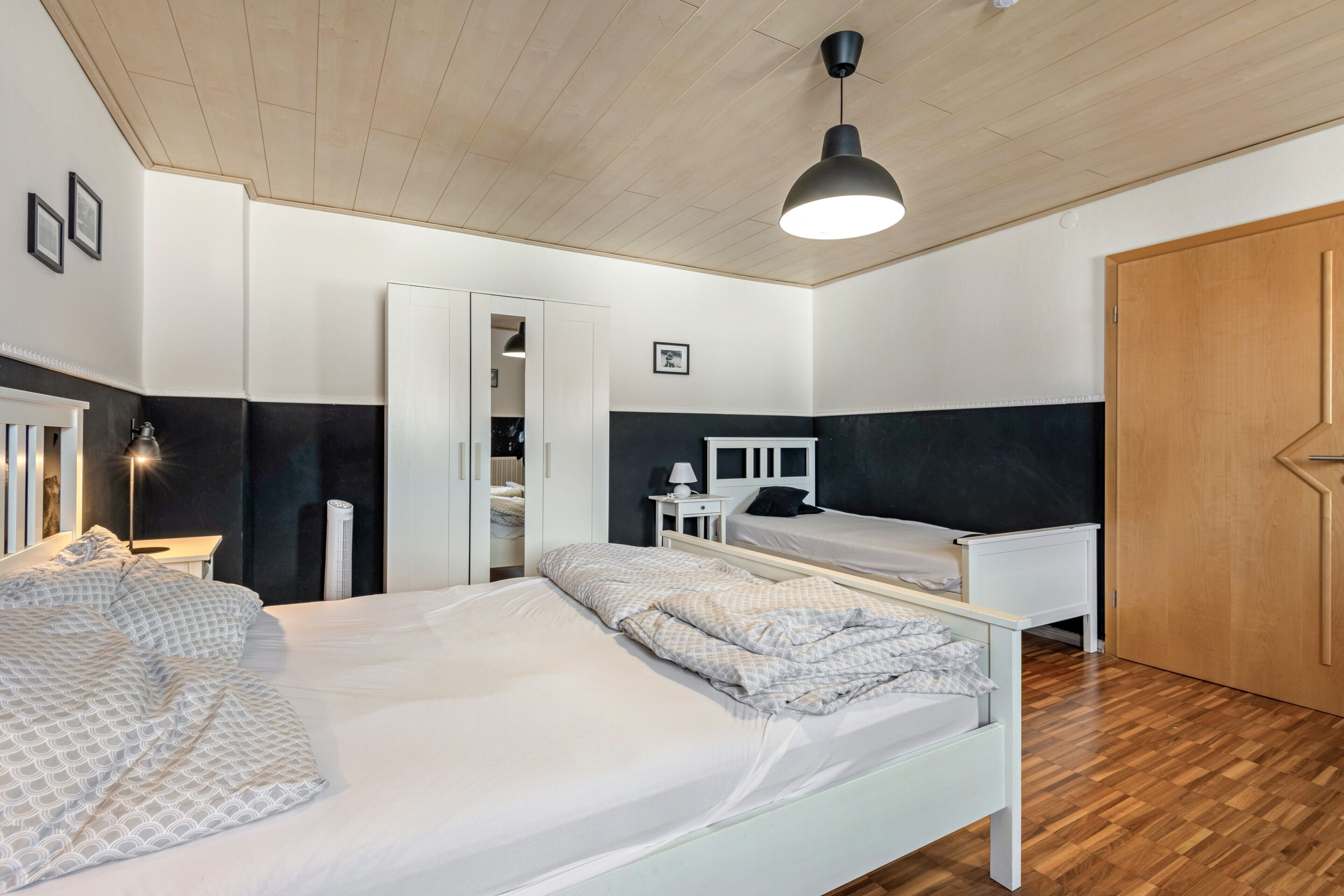A bedroom with two beds, a wardrobe, a bedside table with a lamp, and a ceiling light.