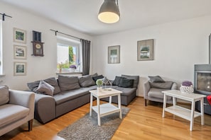 A modern living room with a grey sofa, two white side tables, a grey armchair, and a large window with curtains. - Holiday Home 'Am Limes' with Private Terrace, Private Garden and Wi-Fi (Altmannstein)
