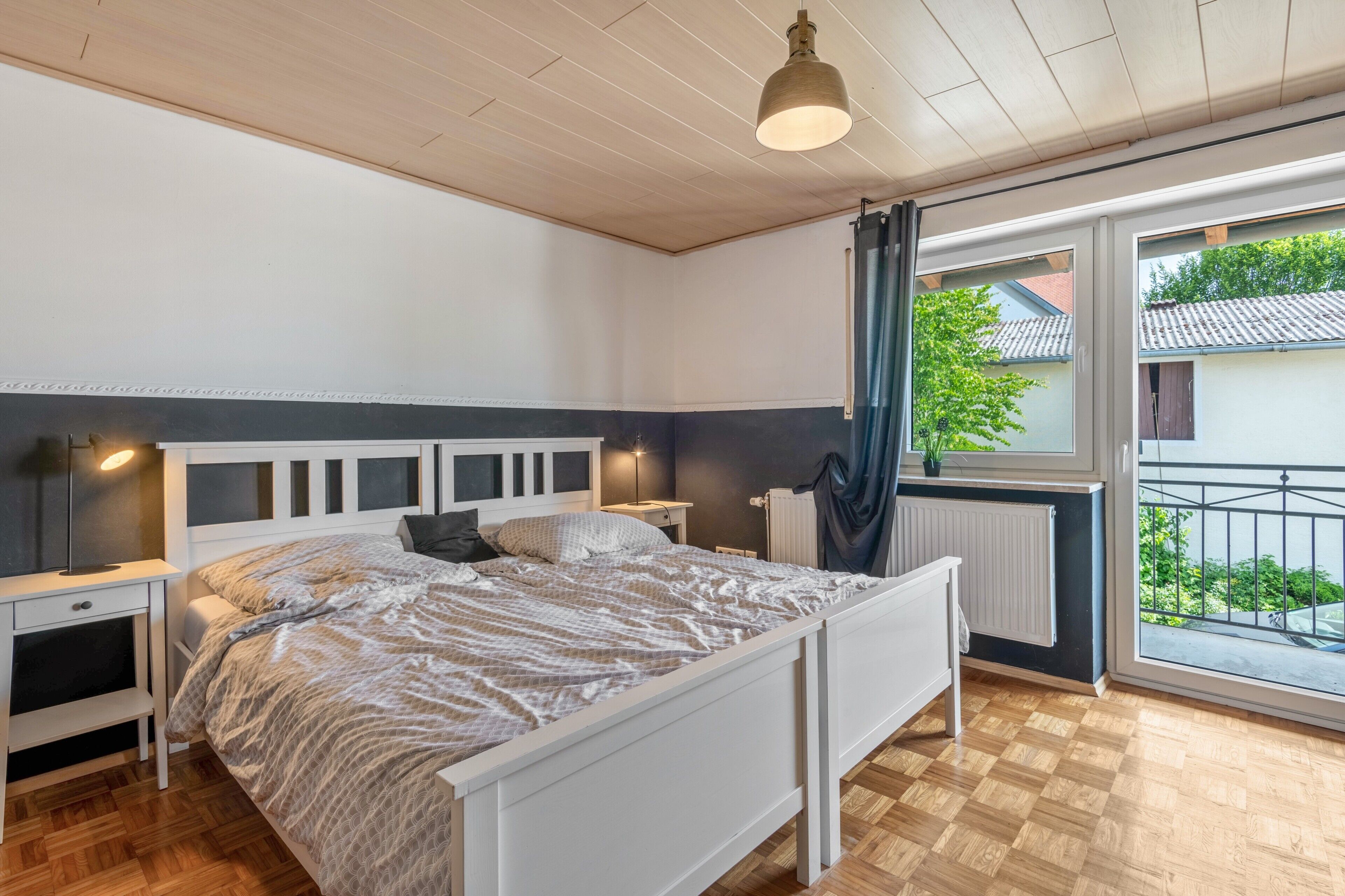 A bedroom with a bed, bedside tables, a window with a view, and a ceiling light.