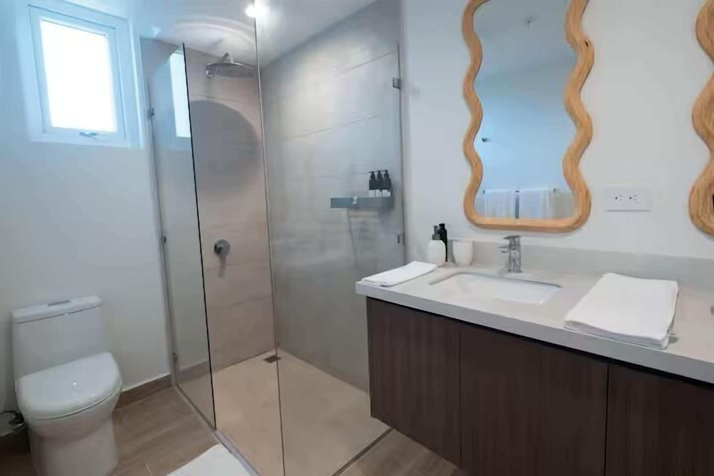 A modern bathroom with a glass shower enclosure, a vanity with two sinks, and a large mirror with a wavy frame.