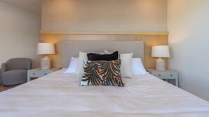 A hotel room with a large bed, two bedside tables with lamps, a chair, and a decorative pillow. - Pacific Point 1106B (Jaco)