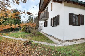 Un bâtiment blanc doté d’un balcon, d’un chemin de pierre et d’une zone herbeuse parsemée de feuilles mortes.