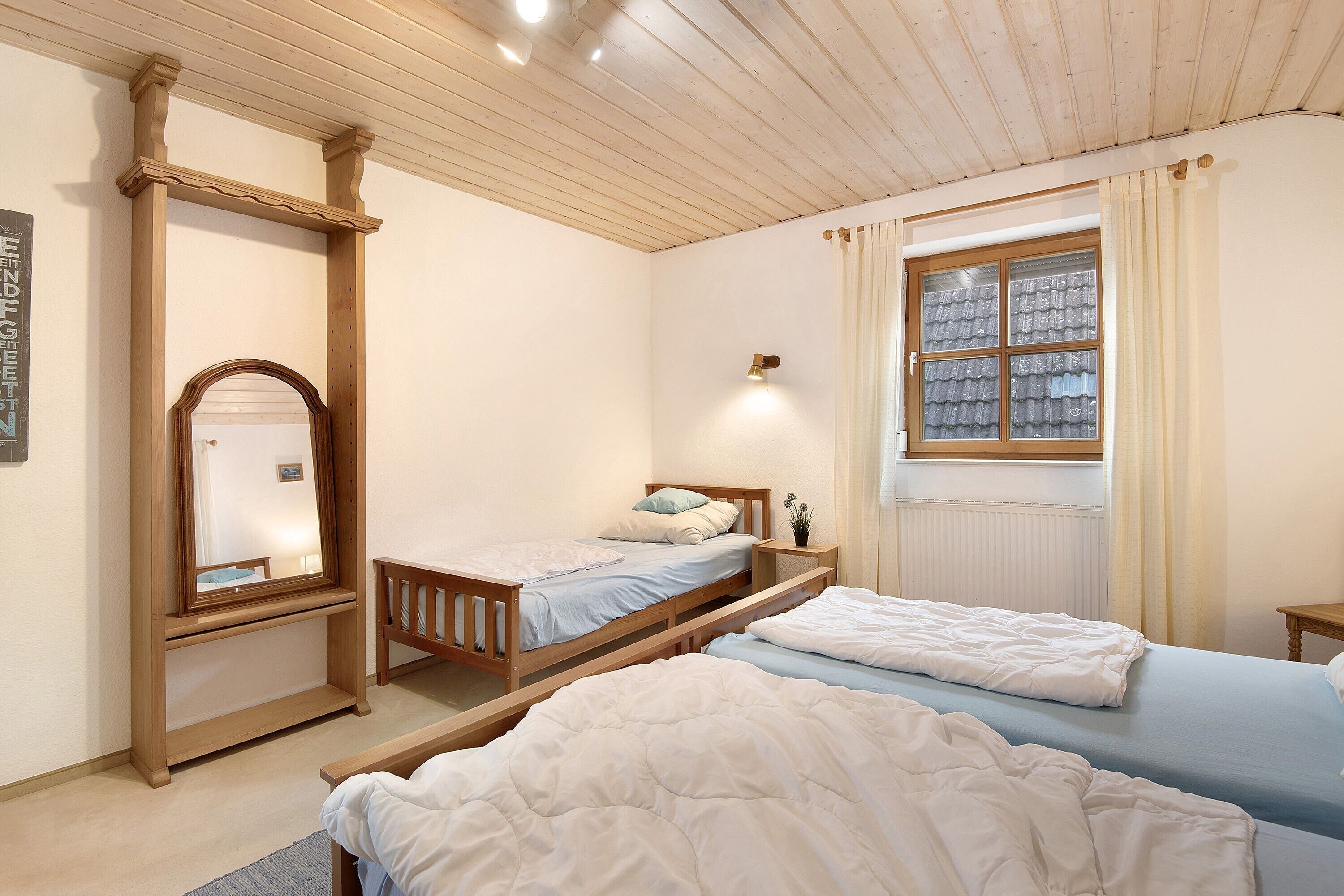 Un dormitorio con dos camas, cabeceros de madera, mesitas de noche, un espejo y una ventana con cortinas.
