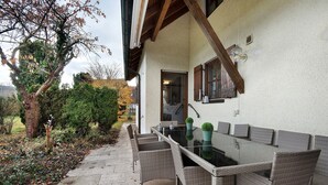 An outdoor dining area with a glass table and wicker chairs, a wooden beam ceiling, and a white exterior wall. - Holiday Home 'Landhaus in Pförring' with Balcony and Wi-Fi (Pförring)