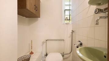 A small bathroom with a toilet, a green sink, a wooden cabinet, a window, and a radiator.