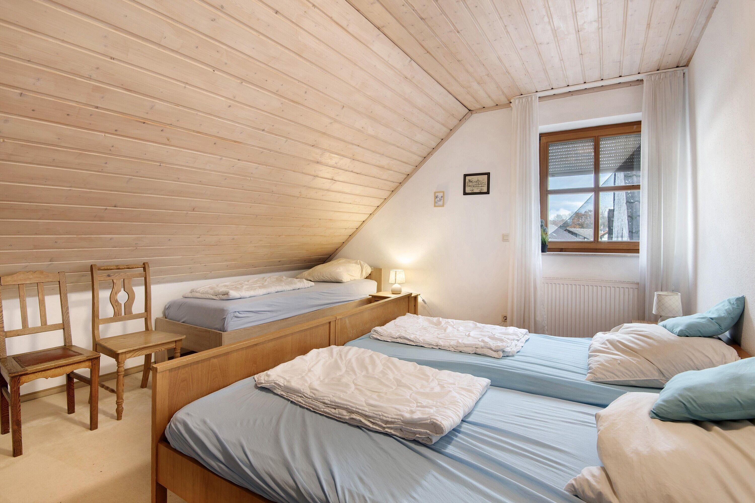 A bedroom with two beds, a wooden desk, and a window with curtains.