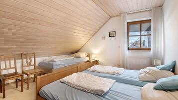 A bedroom with two beds, a wooden desk, and a window with curtains.