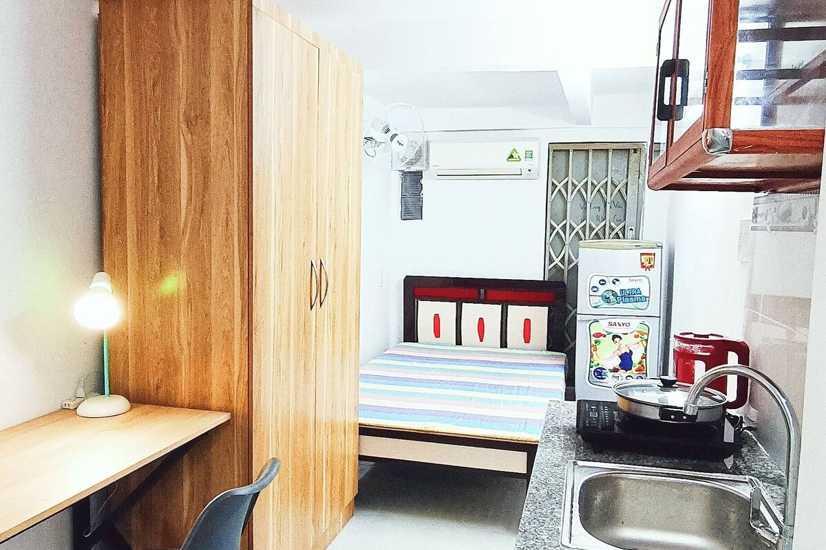 A compact room with a bed, a desk, a chair, a kitchenette, and a wardrobe.