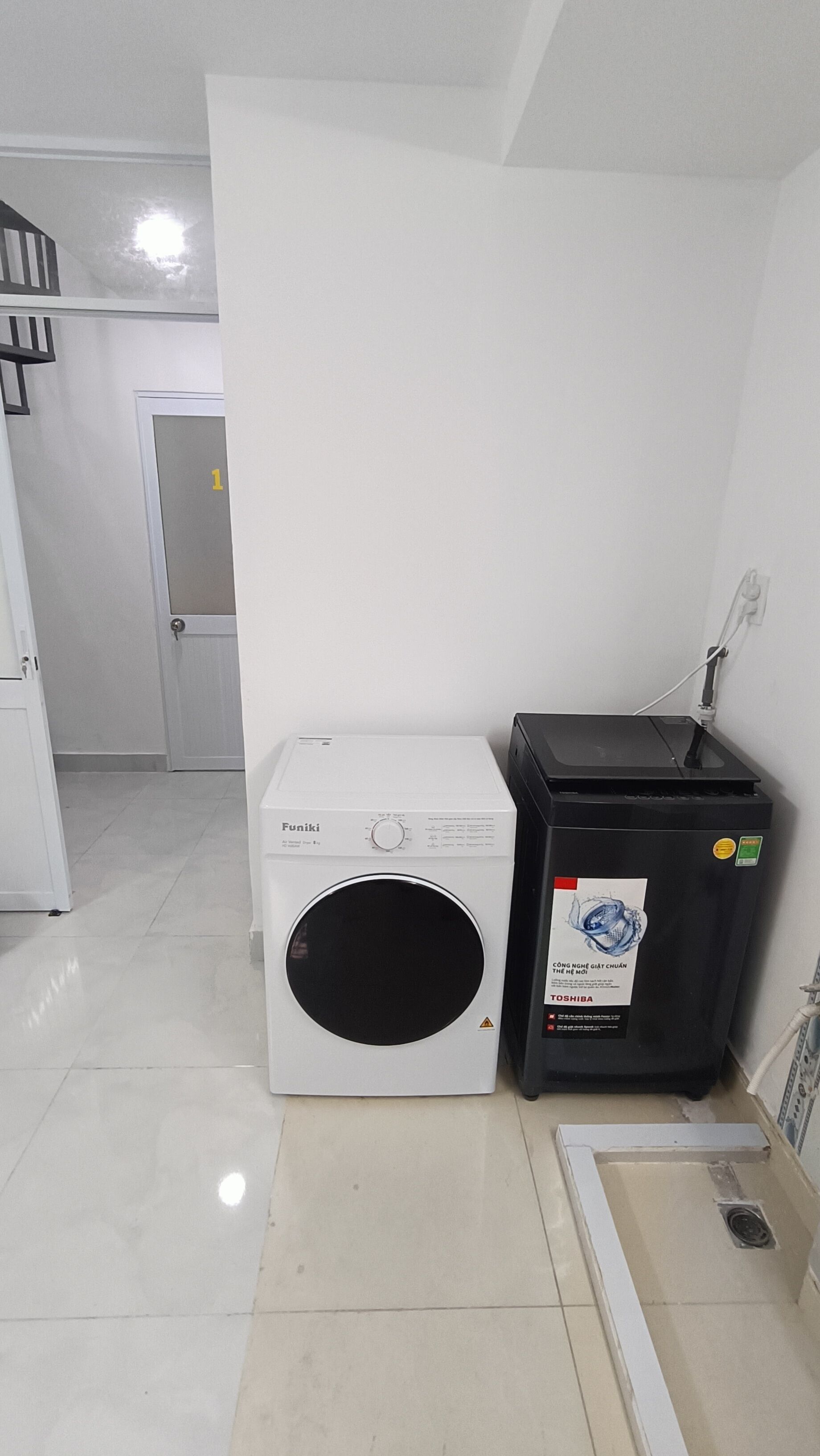 A compact room with a white washing machine, a black recycling bin, and a white door.