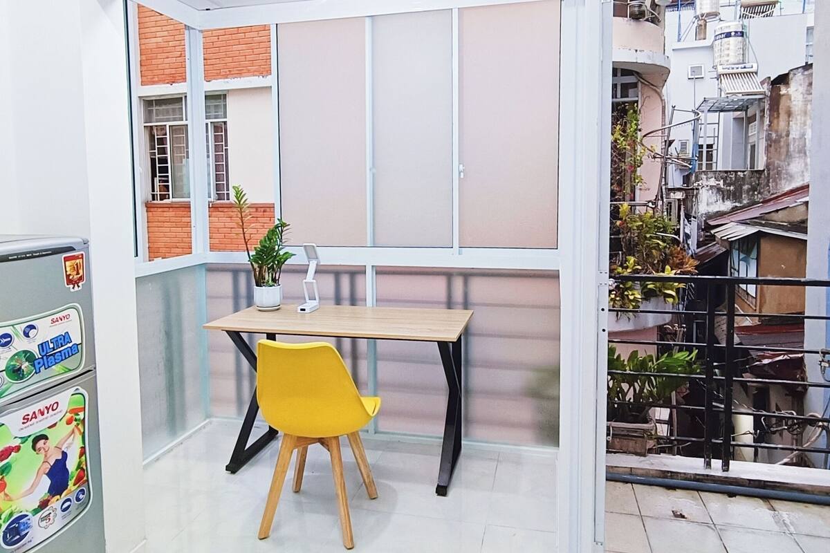 A small room with a window, a table, a yellow chair, and a refrigerator.